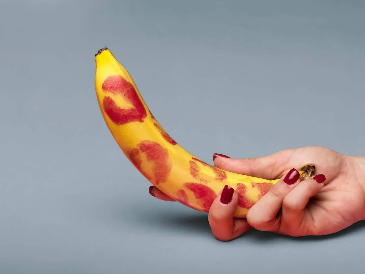 A hand holding a banana with red lipstick marks. Explore natural ways to manage erectile dysfunction for Filipino men at andyou.ph.